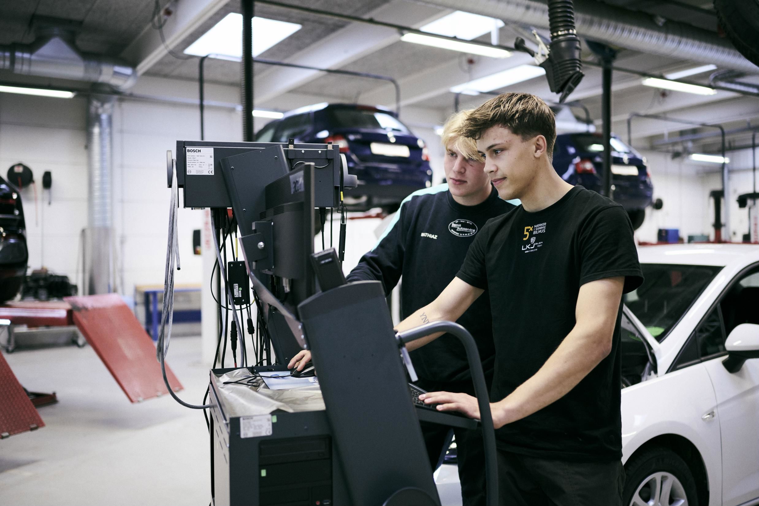 Et par mekanikerlærlinge bruger skolens testudstyr på autoværkstedet.