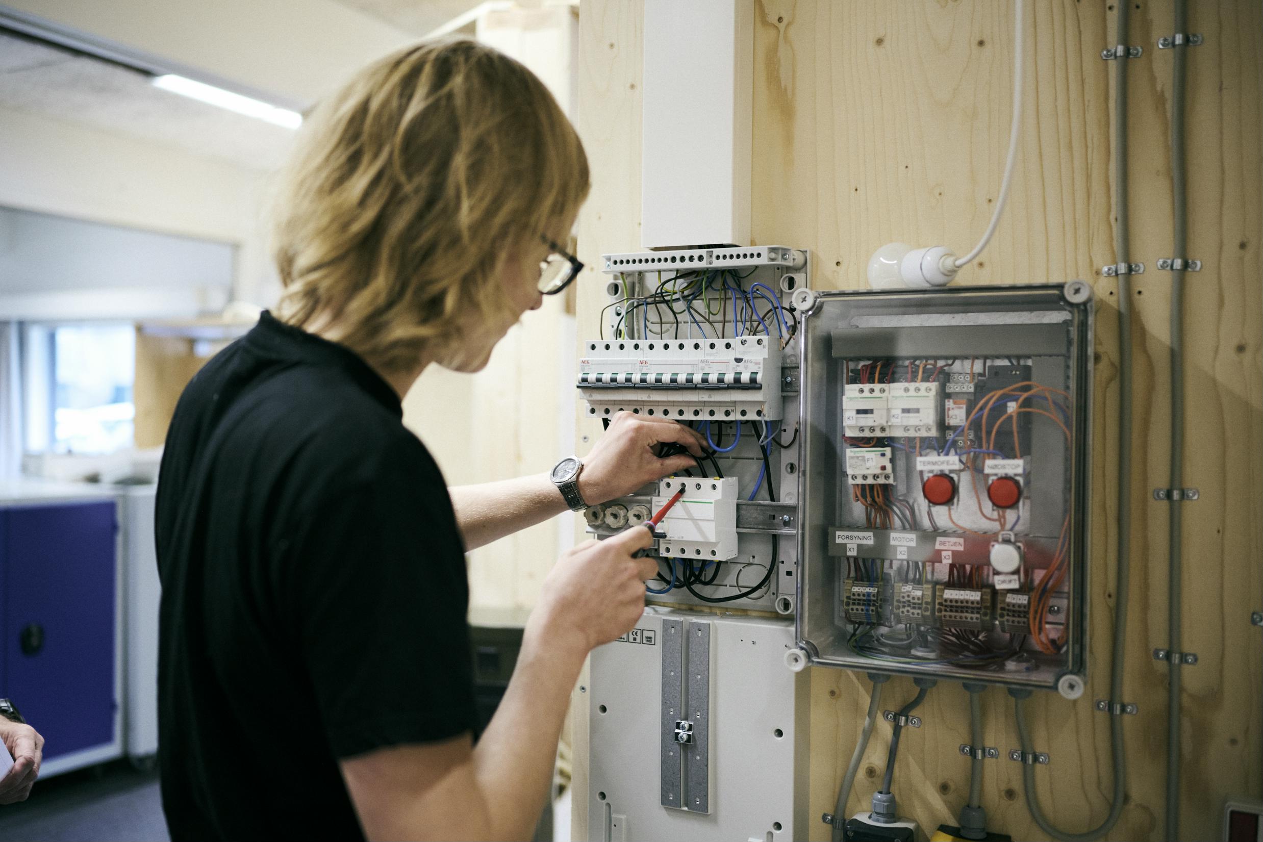 En elev på skolens elværksted er ved at tilslutte en eltavle.