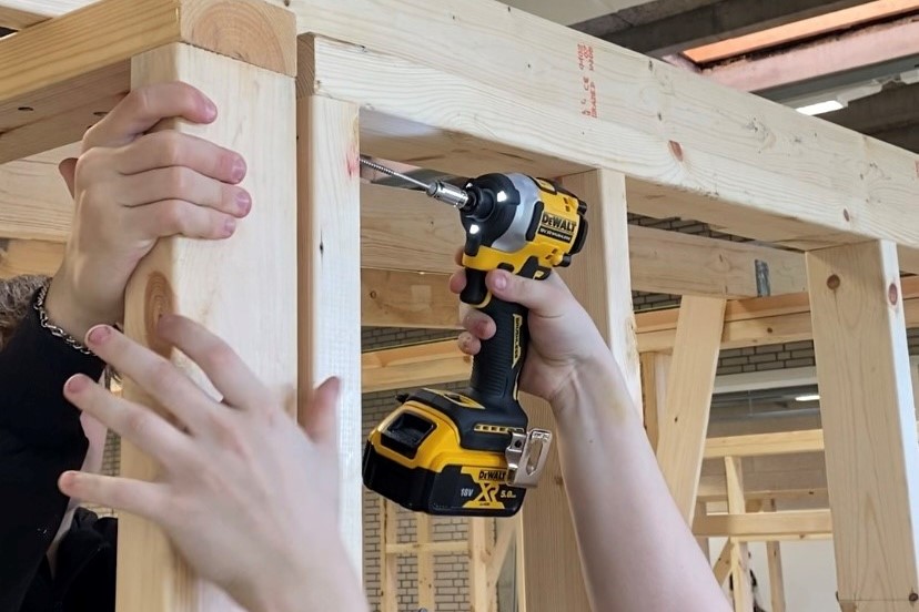 To tømrerelever på Hansenbergs værksted skruer et træskelet sammen til en hytte.