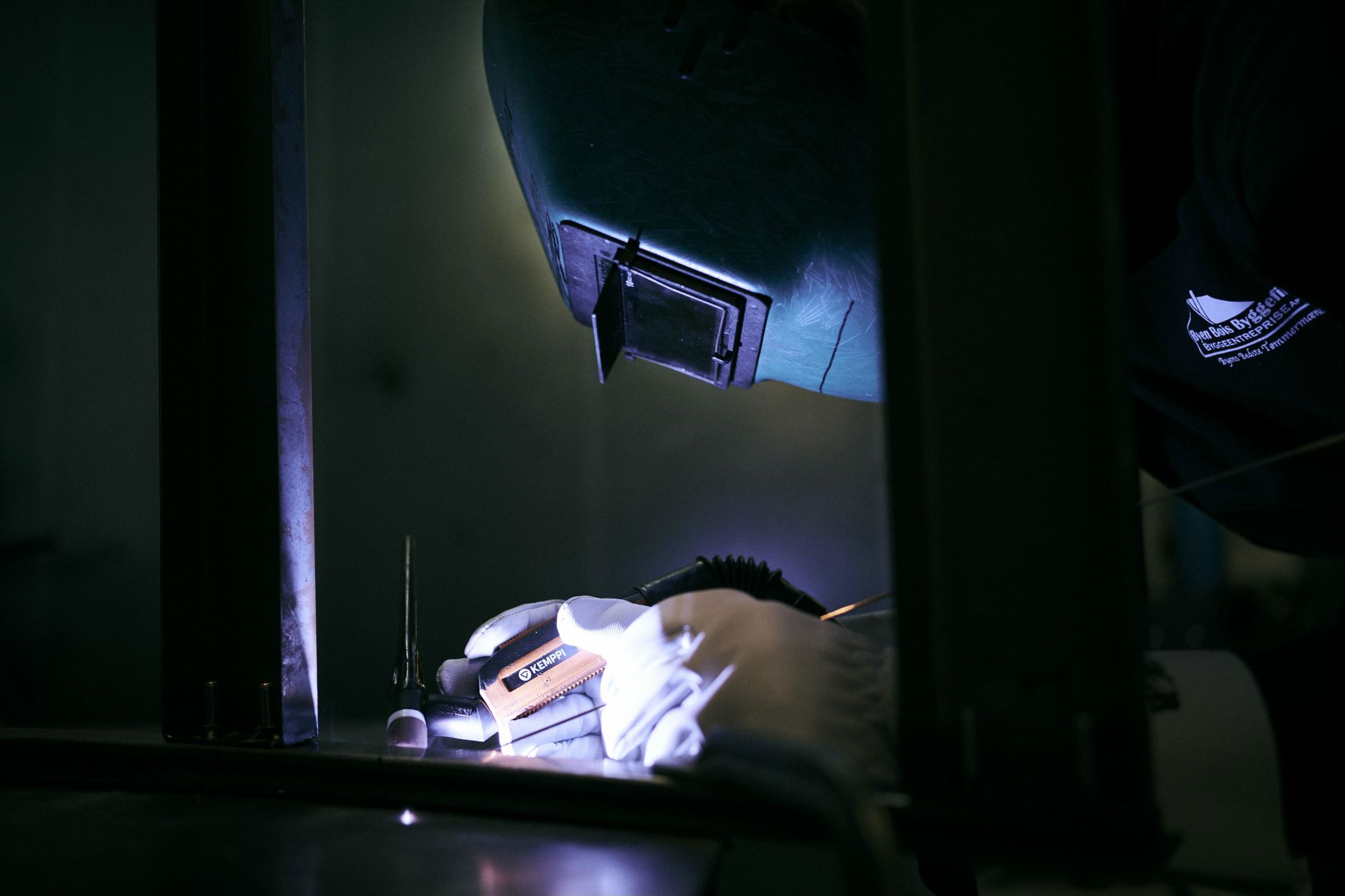 En lærling på skolens smedeværksted, med ansigtet gemt bag svejsehjelmen, er i færd med at svejse.