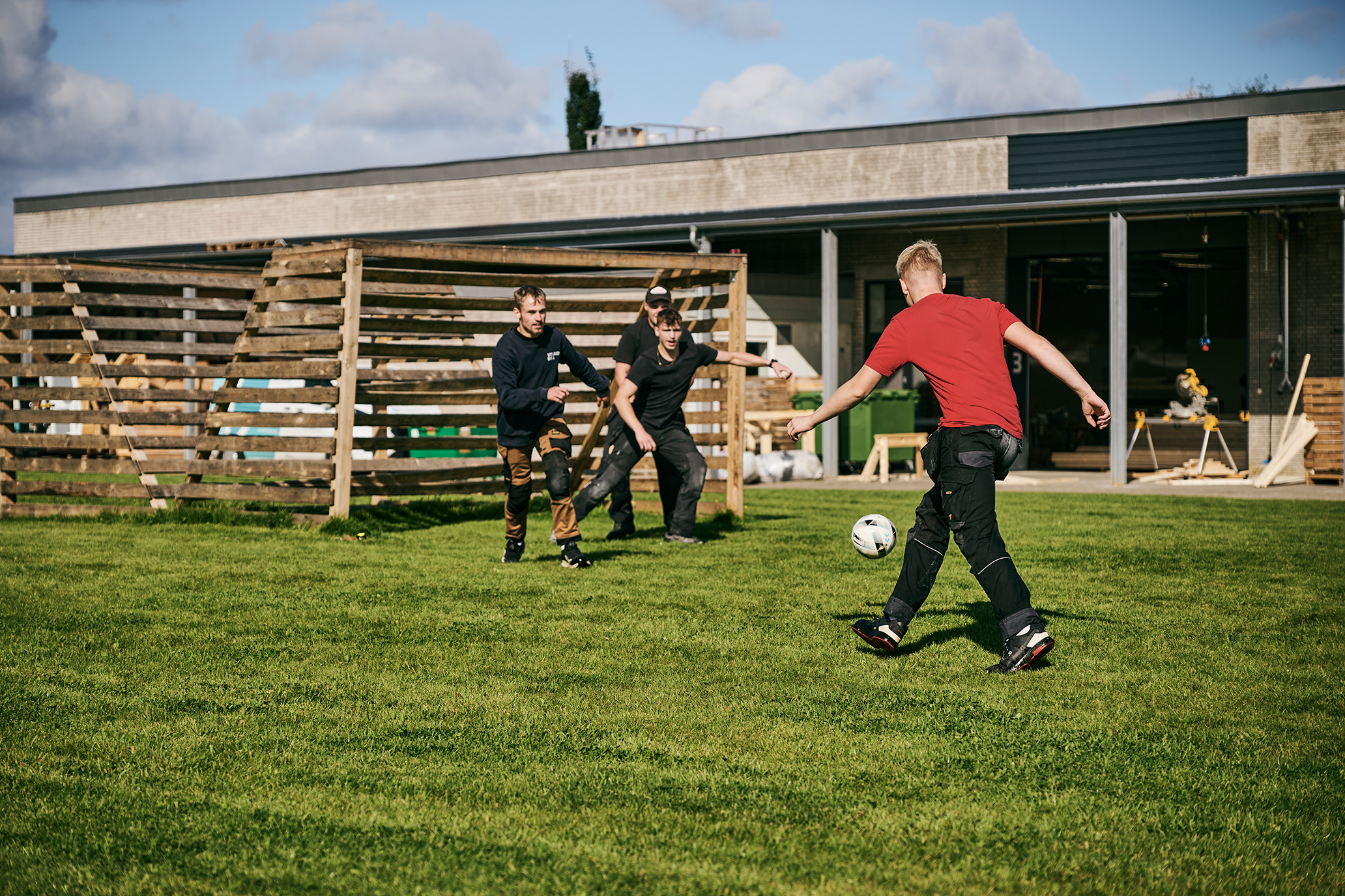 Nogle tømrerlærlinge spiller fodbold udenfor tømrerværkstedet, hvor også deltagerne i Byg og Ræs kan boltre sig.