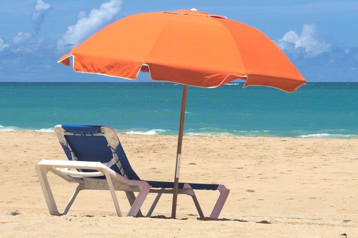 Sommer og strand, en liggestol i strandkanten med en orange parasol.