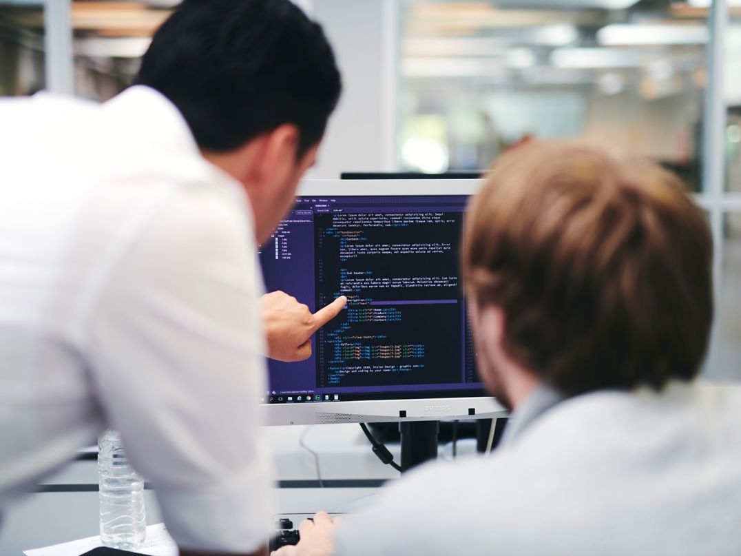 En lærer underviser en webudviklerelev i kodning på en computerskærm.