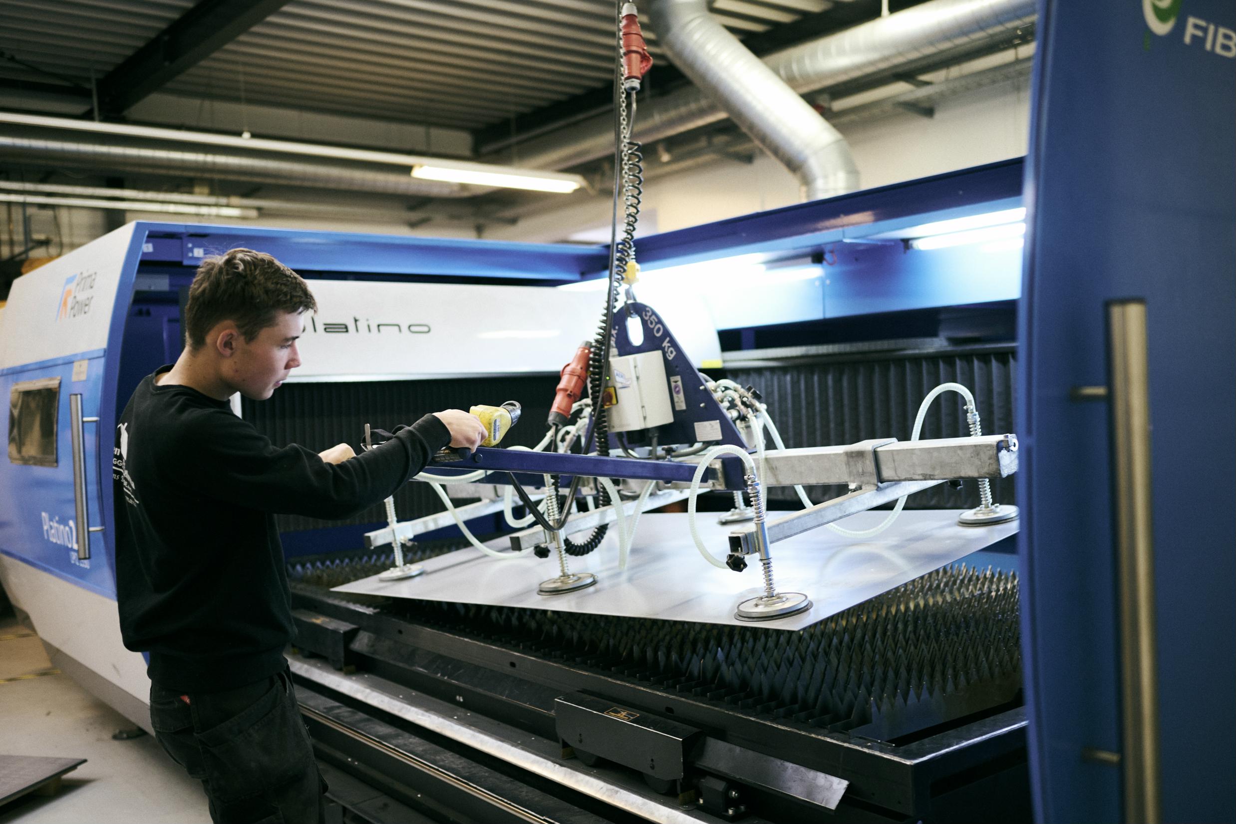 En smedeelev hejser en jernplade op og placerer den i den store fiberlaser på Hansenbergs smedeværksted.