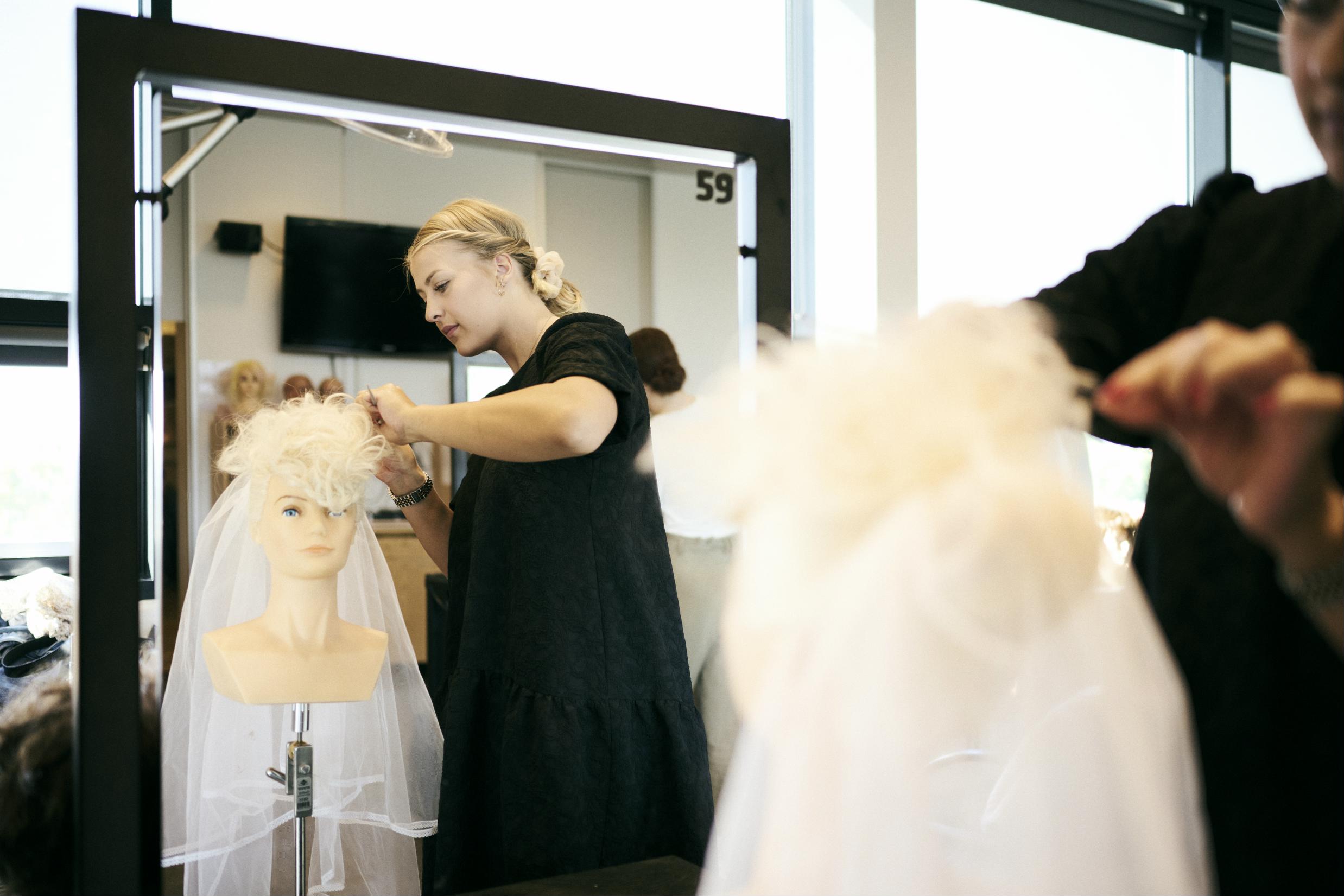 Frisørelev på Hansenberg sætter håret op til en brudefrisure på et øvelseshoved.