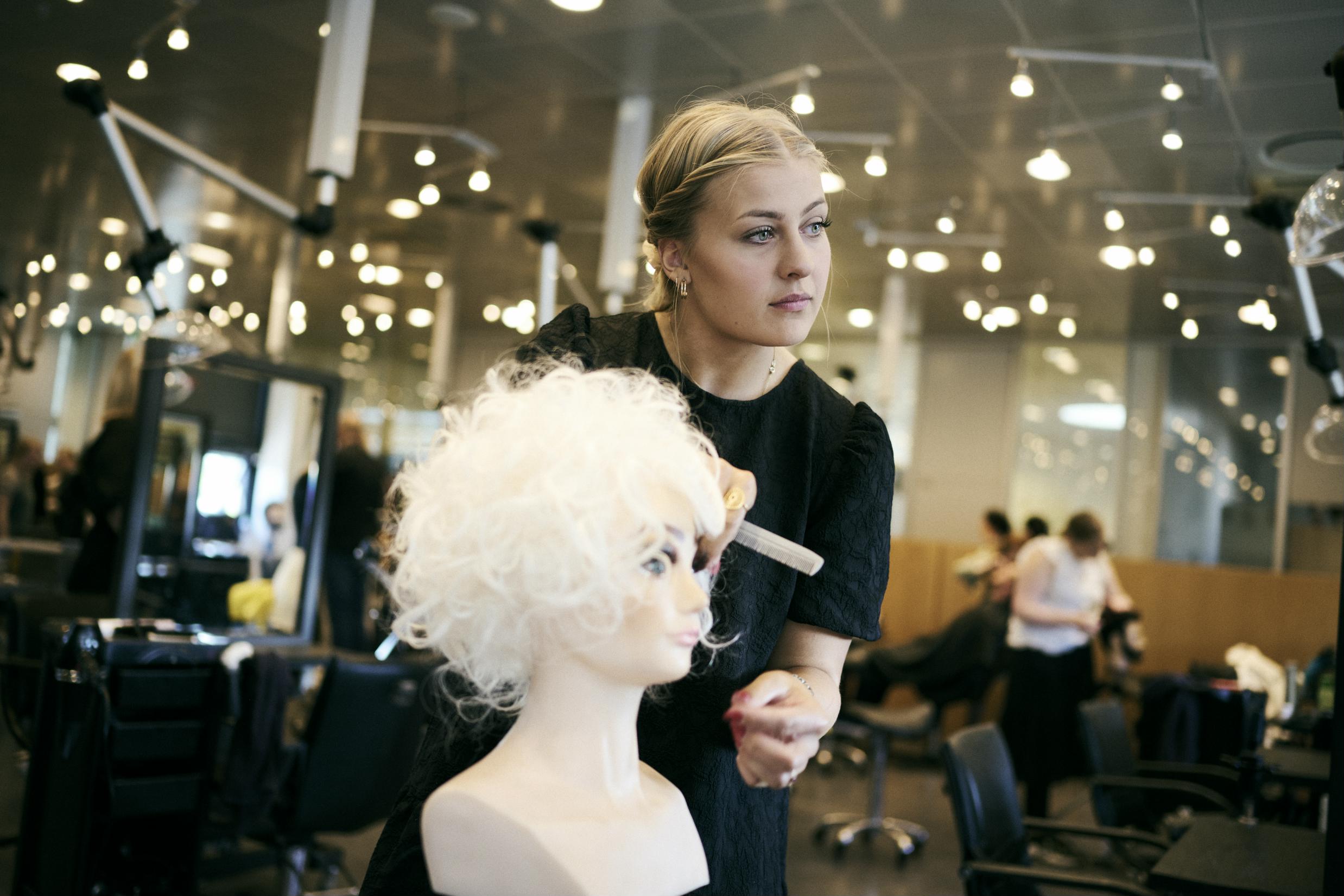 Frisørelev på Hansenberg retter på krøllerne på et øvelseshoved