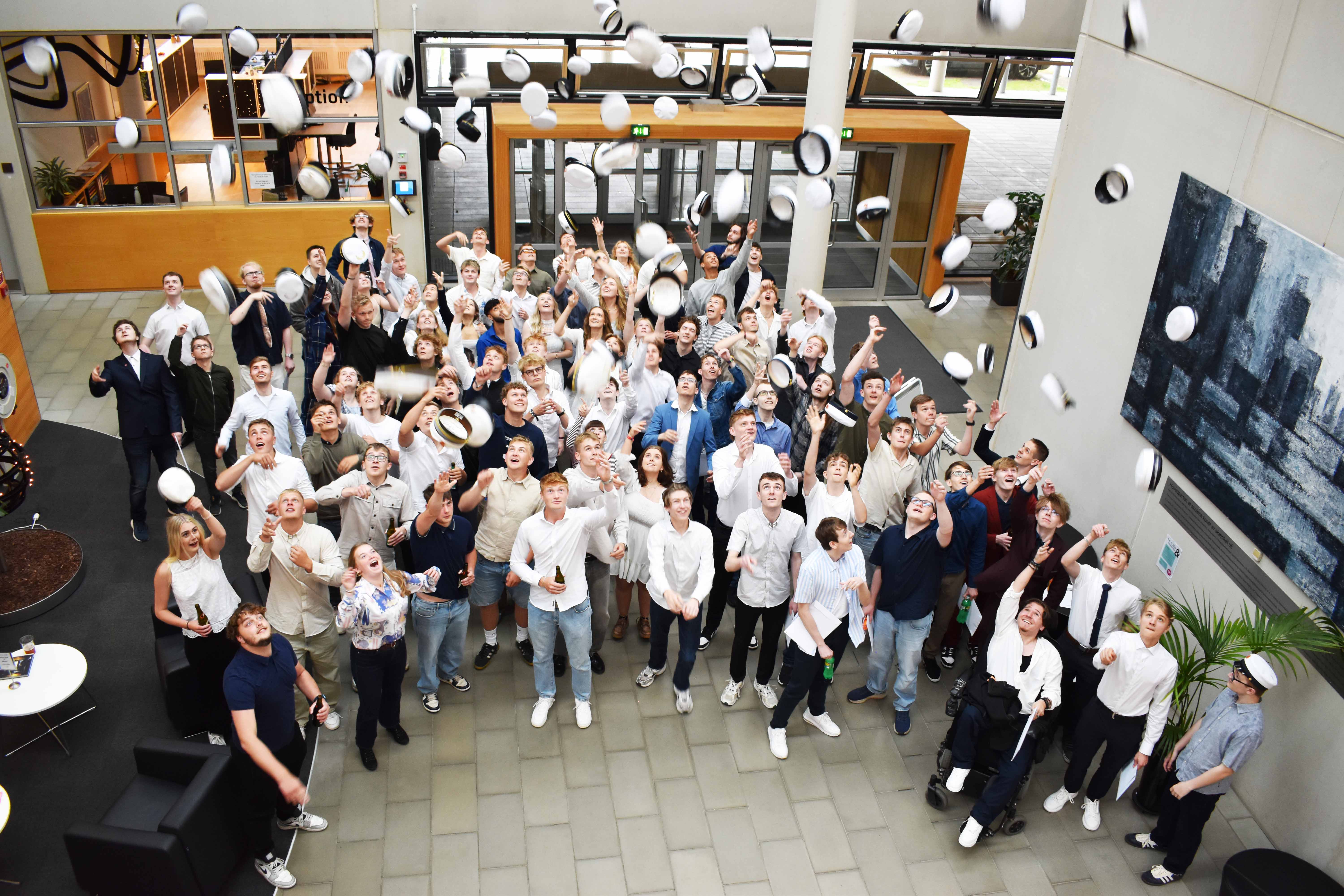 En flok glade HTX- og EUX-studenter fejrer studenterhuen ved at kaste den op i luften.