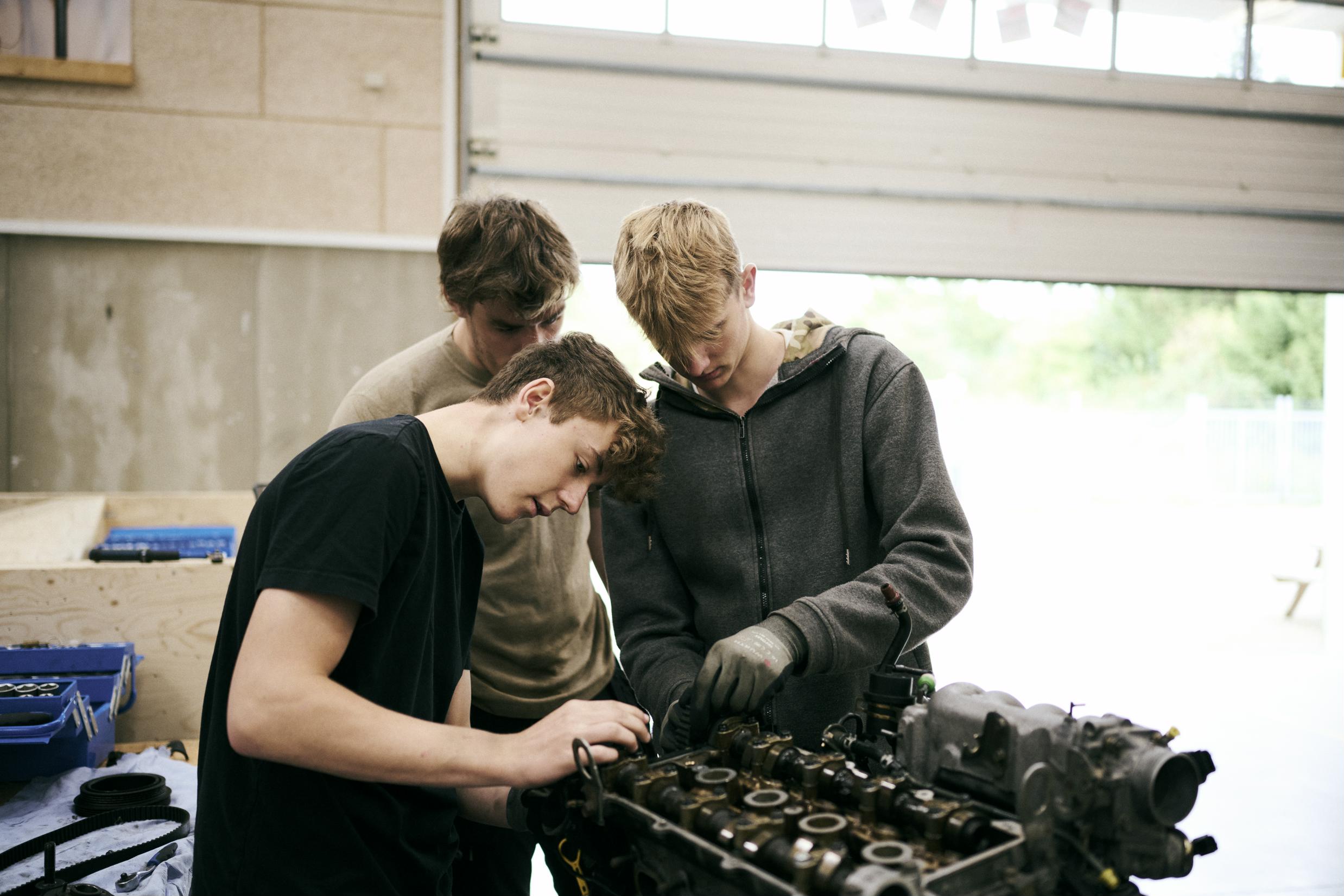 Tre mekanikerelever på Grundforløb 1 arbejder på en motor på et af skolens værksteder.