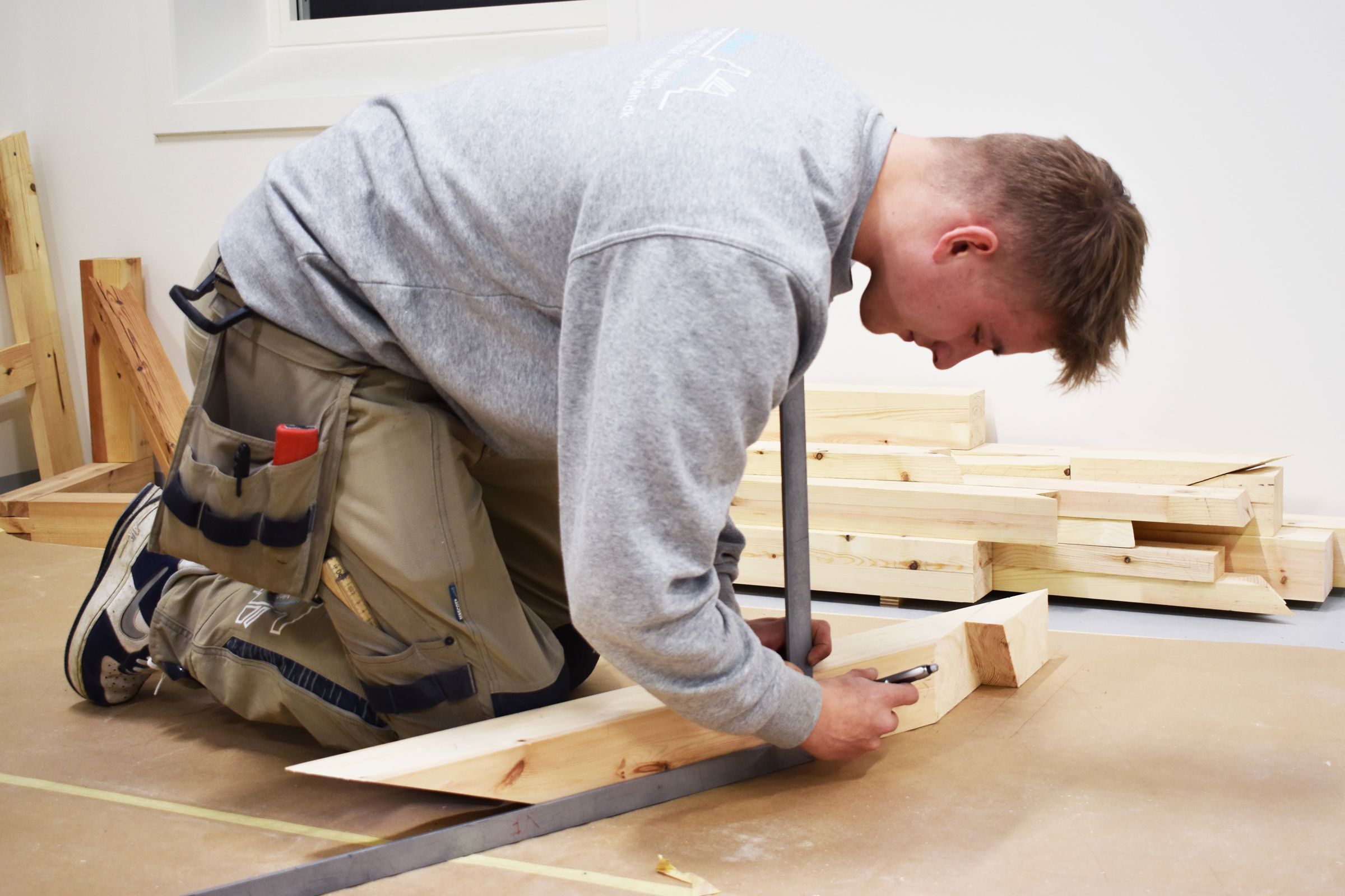 Toke, der er tømrerelev træner til DM i Skills 2024, og tjekker om målene på træet stemmer med tegningerne.