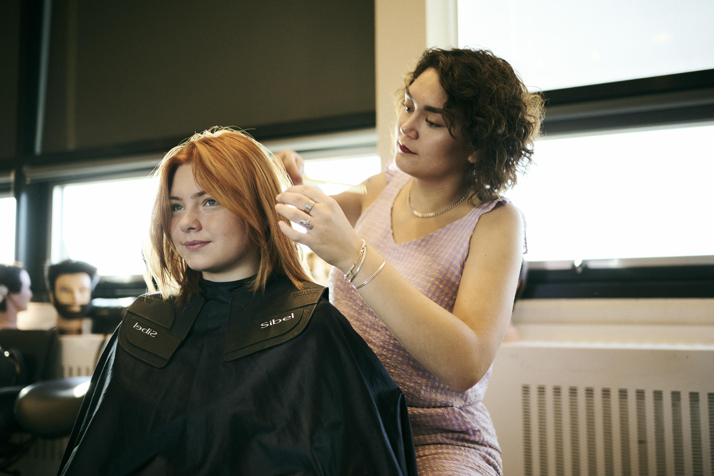 En frisørelev på Hansenberg vurderer håret på en model inden behandlingen.