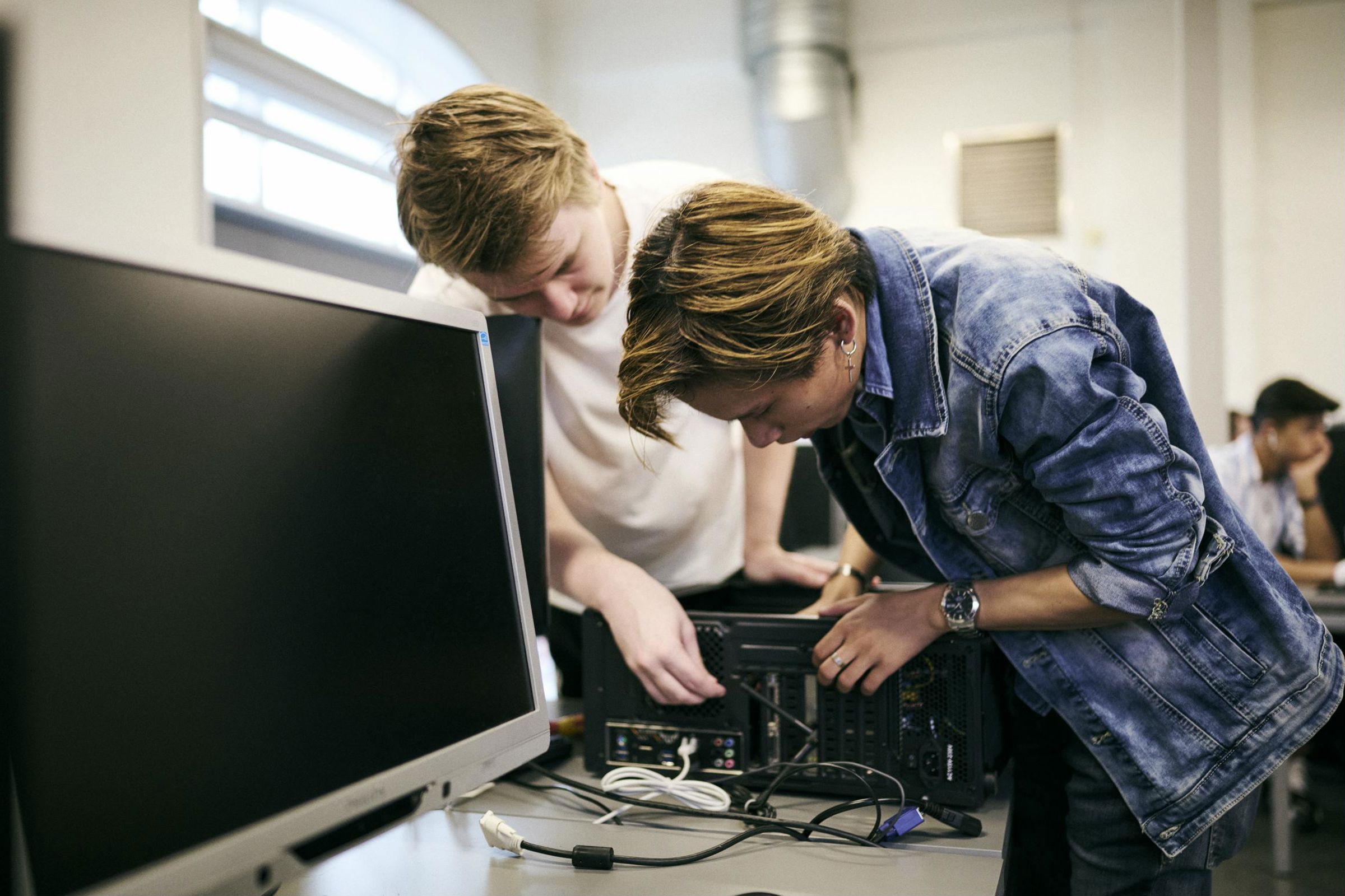 To elever på data- og kommunikationsuddannelsen er ved at sætte kabler i en computer for at skabe et datanetværk.