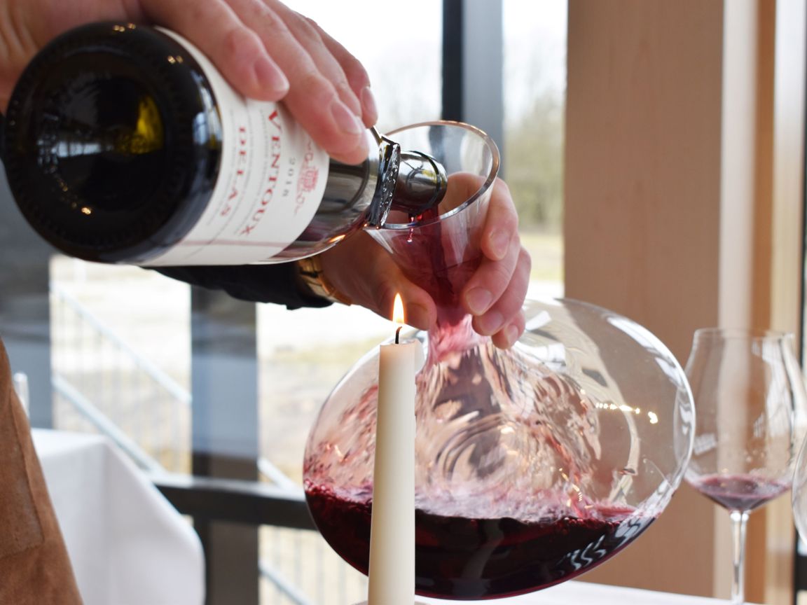 En tjenerelev på skolen dekanterer rødvin i en karaffel over levende lys på Hansenberg.