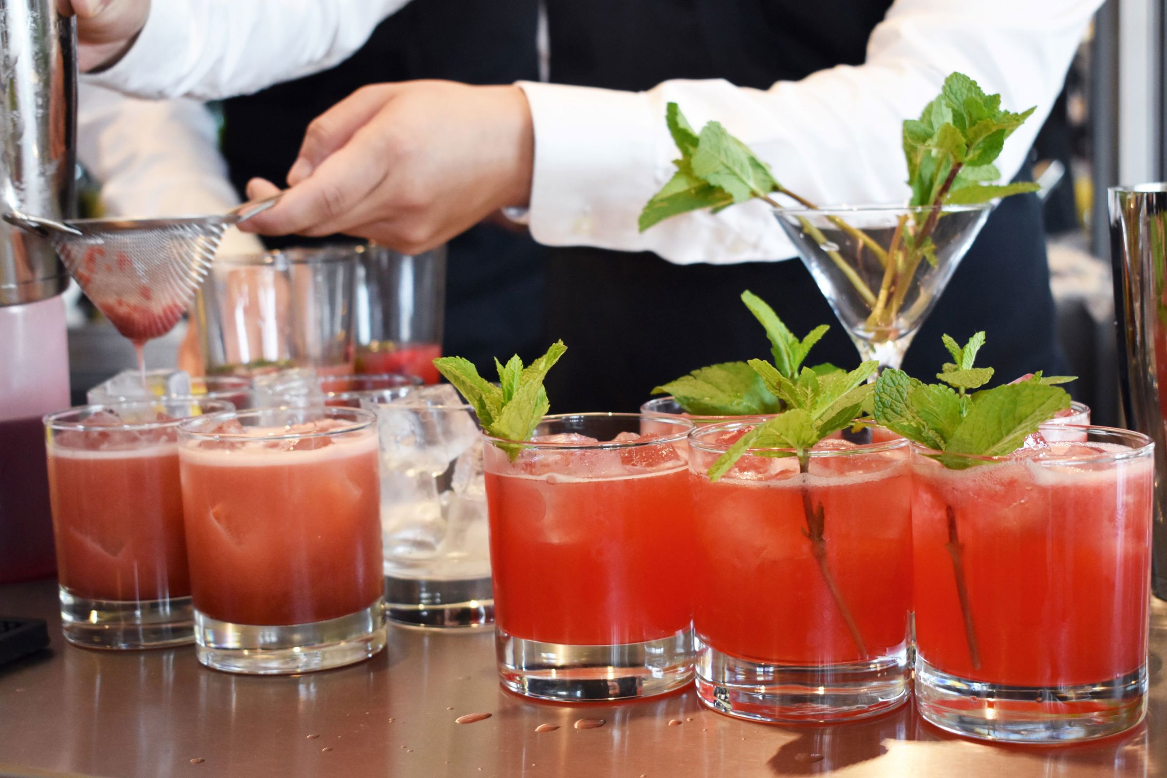 En tjenerelev mixer flotte røde drinks med en kvist af mynte som pynt.