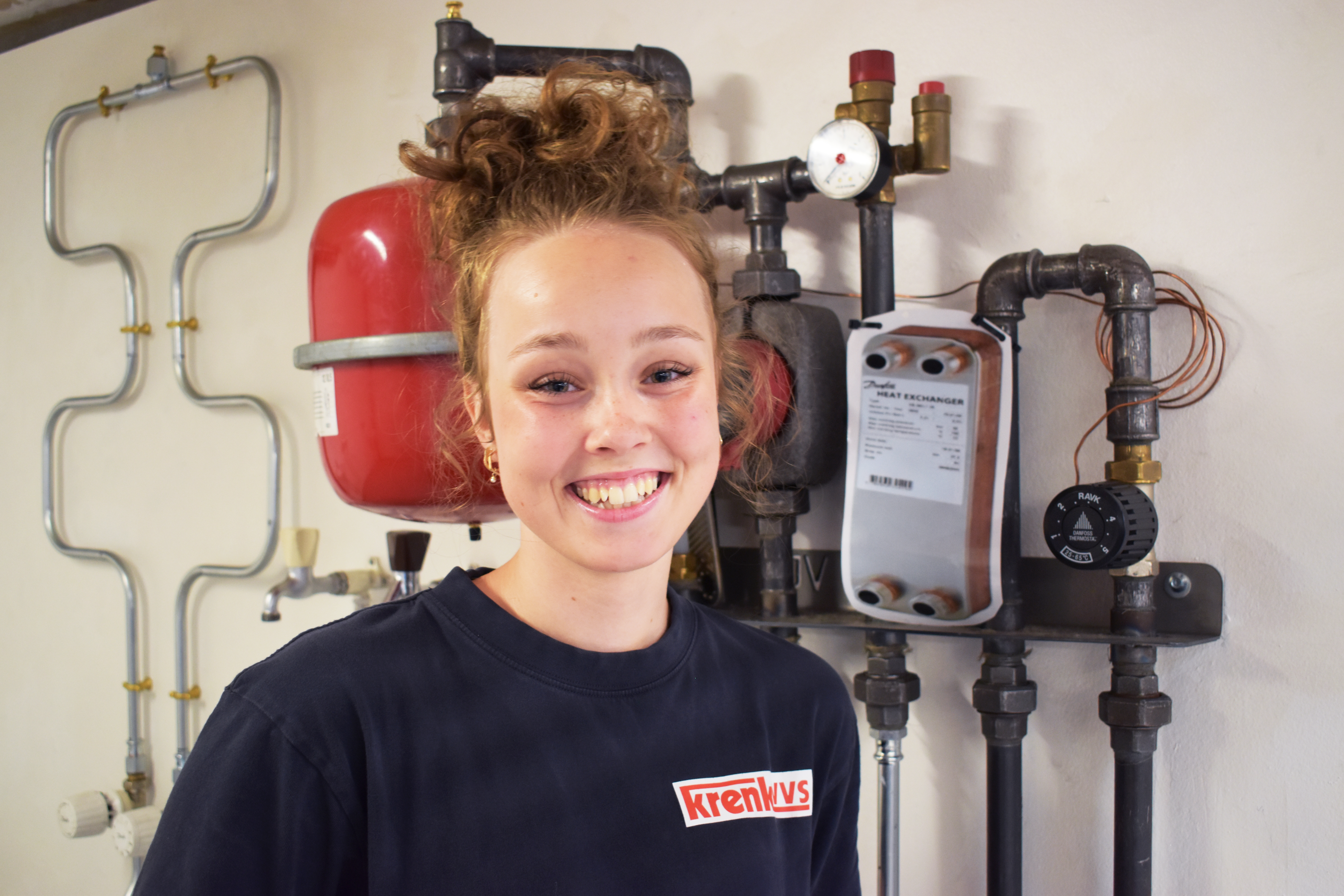 Thea Juul Harder Qvist er i lære som VVS-energispecialist, og hun står her foran en installation i VVS-værkstedet.