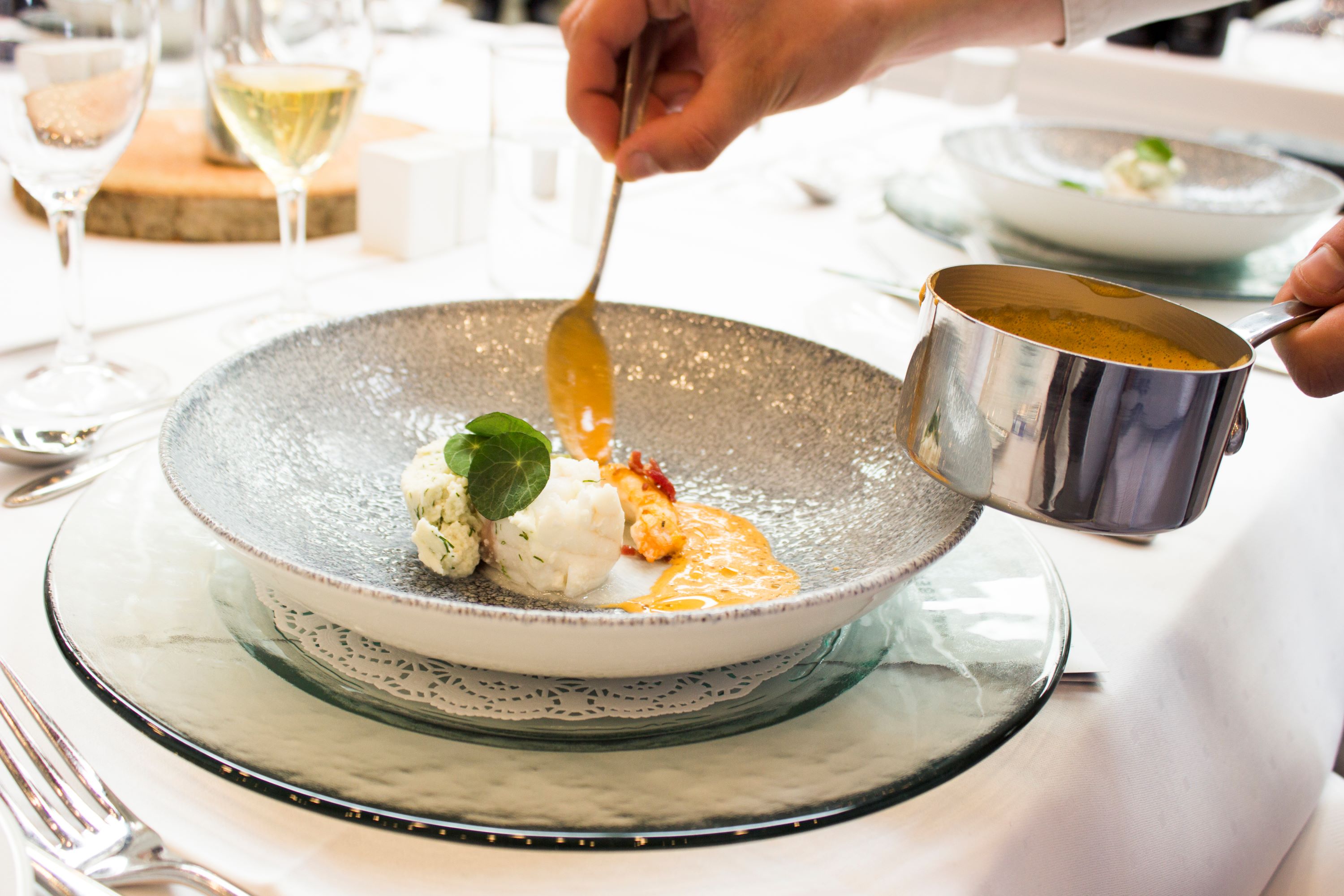 En tjenerelev serverer og hælder sauce op til en gæst i skolens undervisningsrestaurant.